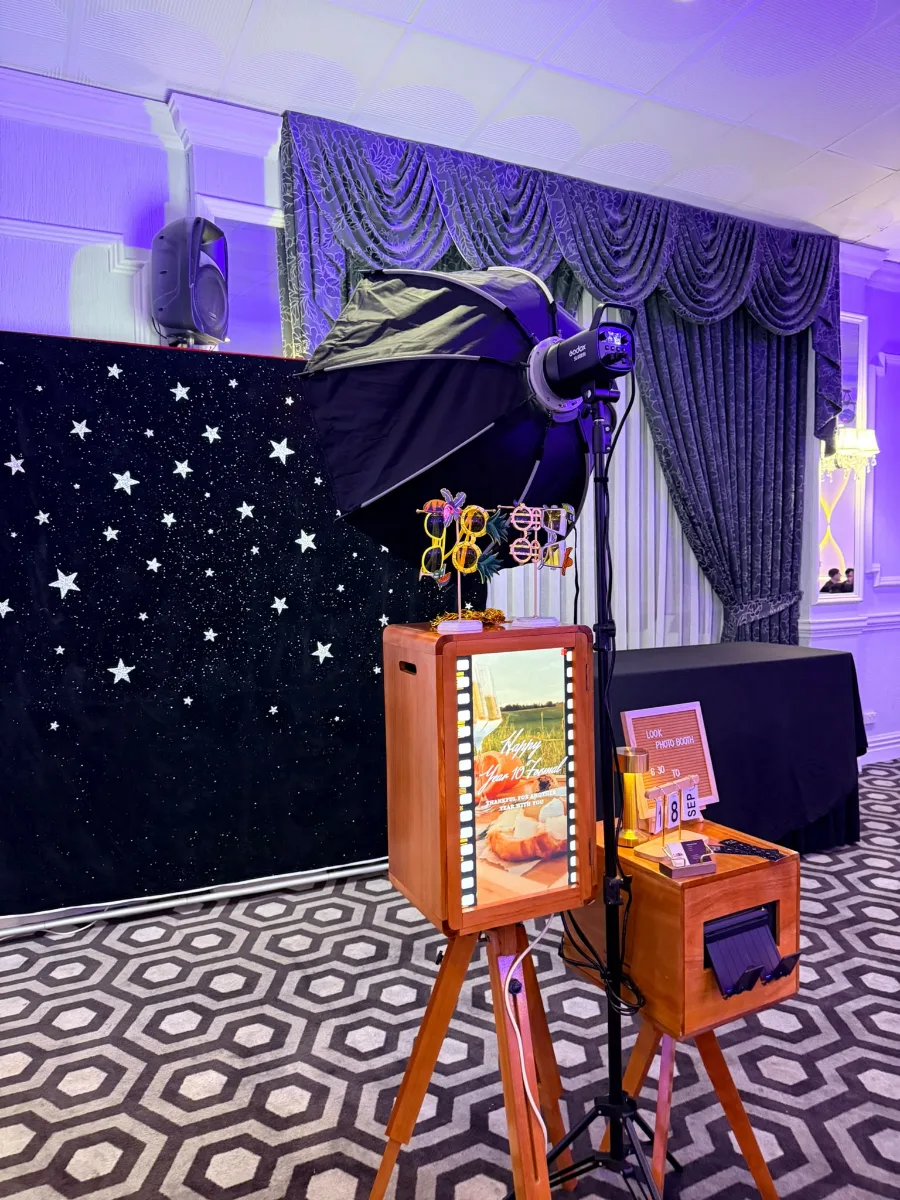 The wooden Look Photobooth and its printer set up in front of a starry backdrop, with props on top